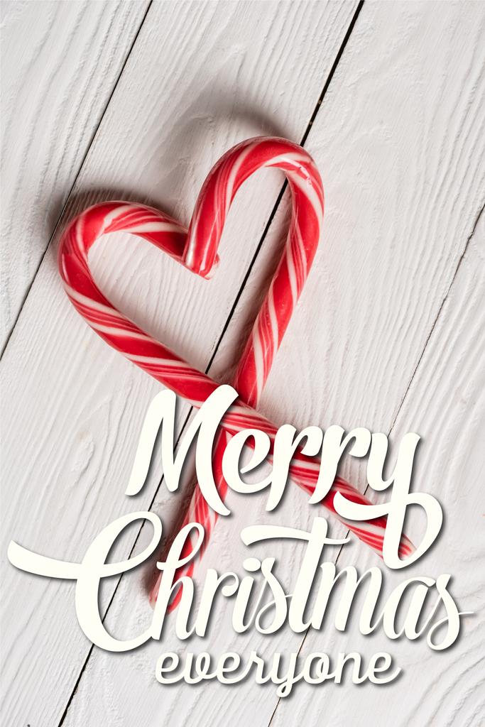 Kalp şeklinde baston şekerlerin en üst görüntüsü ahşap arka planda neşeli Noel yazıları. - Fotoğraf, Görsel