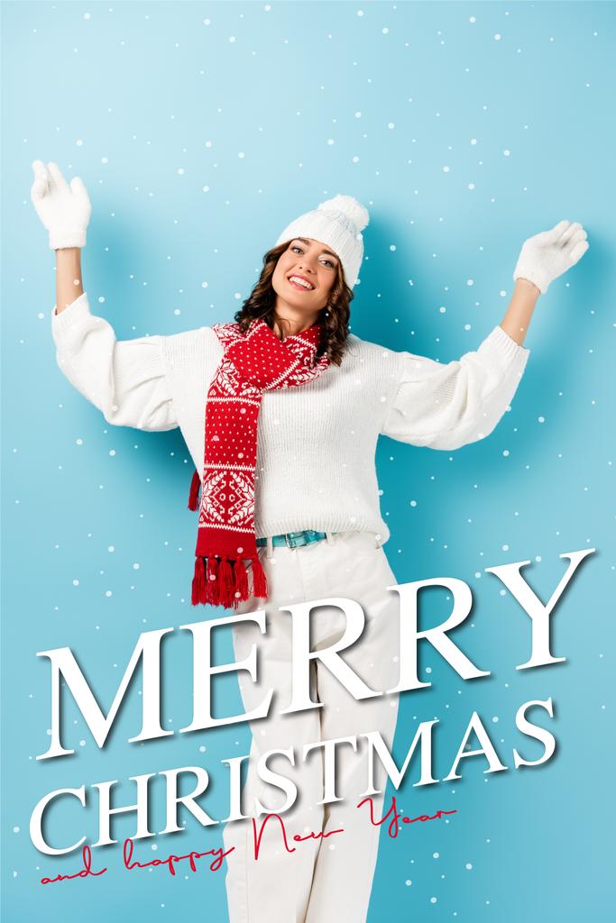 joyful woman in winter outfit, warm scarf, gloves and hat standing with outstretched hands near merry christmas and happy new year lettering on blue - Photo, Image