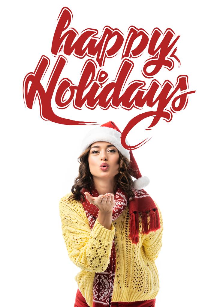 young woman in santa hat and scarf sending air kiss near happy holidays lettering on white  - Photo, Image