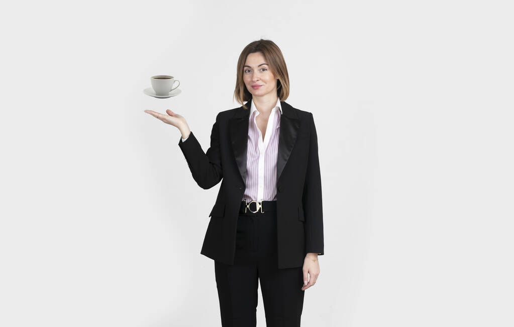 Mujer de negocios en traje negro demostrando una taza de café aislado en blanco. Relájese concepto de tiempo - Foto, imagen