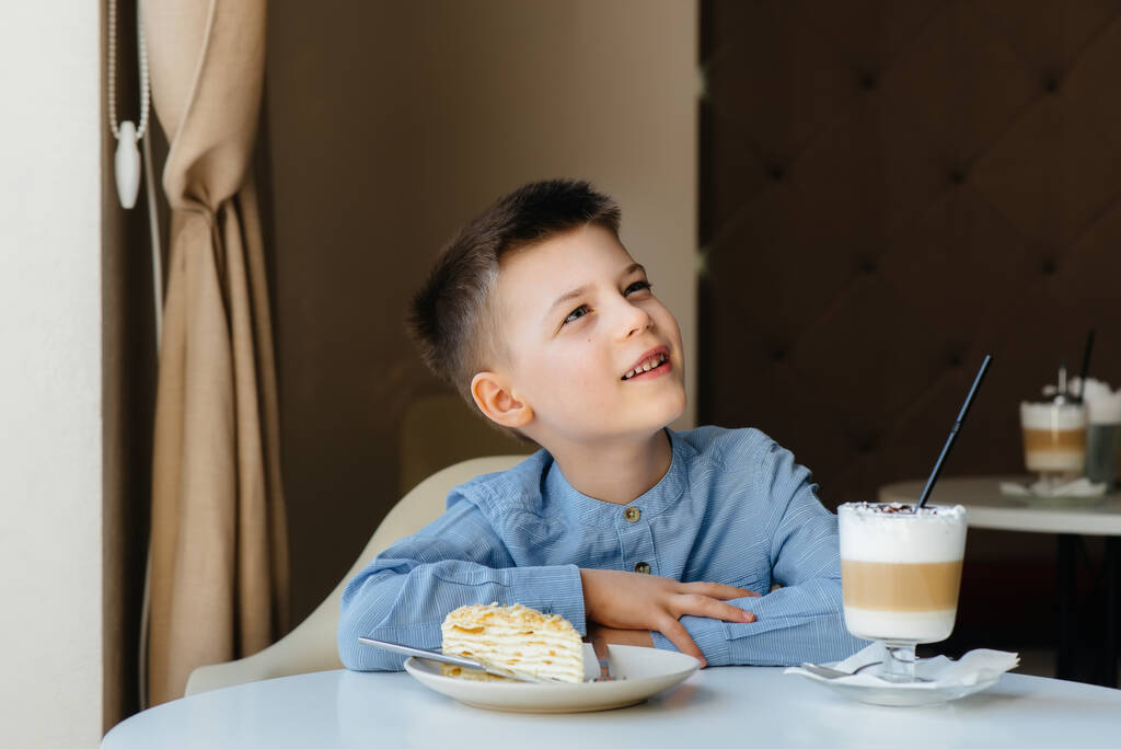 Милый маленький мальчик сидит в кафе и смотрит на торт и какао крупным планом. Диета и правильное питание - Фото, изображение
