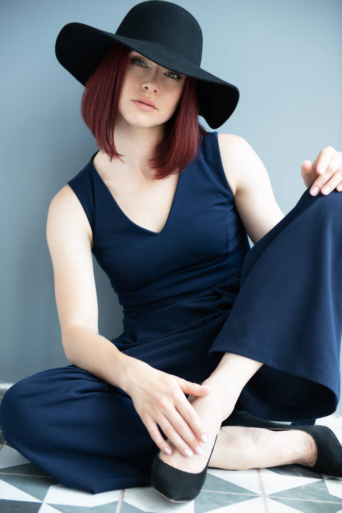 Mujer de moda con ropa azul profundo y sombrero negro posando en interiores  - Foto, Imagen
