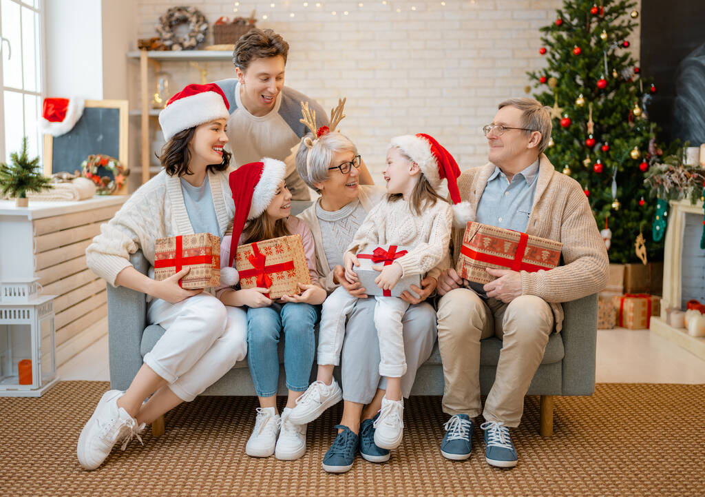 Joyeux Noël et Joyeuses Fêtes ! Grand-mère, grand-père, maman, père et enfants échangeant des cadeaux. Parents et filles s'amusent près d'un arbre à l'intérieur. Famille aimante avec des cadeaux dans la chambre. - Photo, image