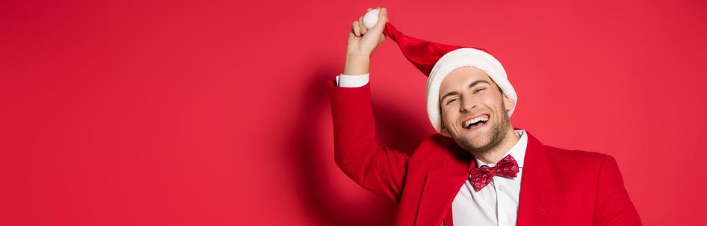 Lächelnder Mann in offizieller Kleidung mit Weihnachtsmütze auf rotem Hintergrund, Banner  - Foto, Bild