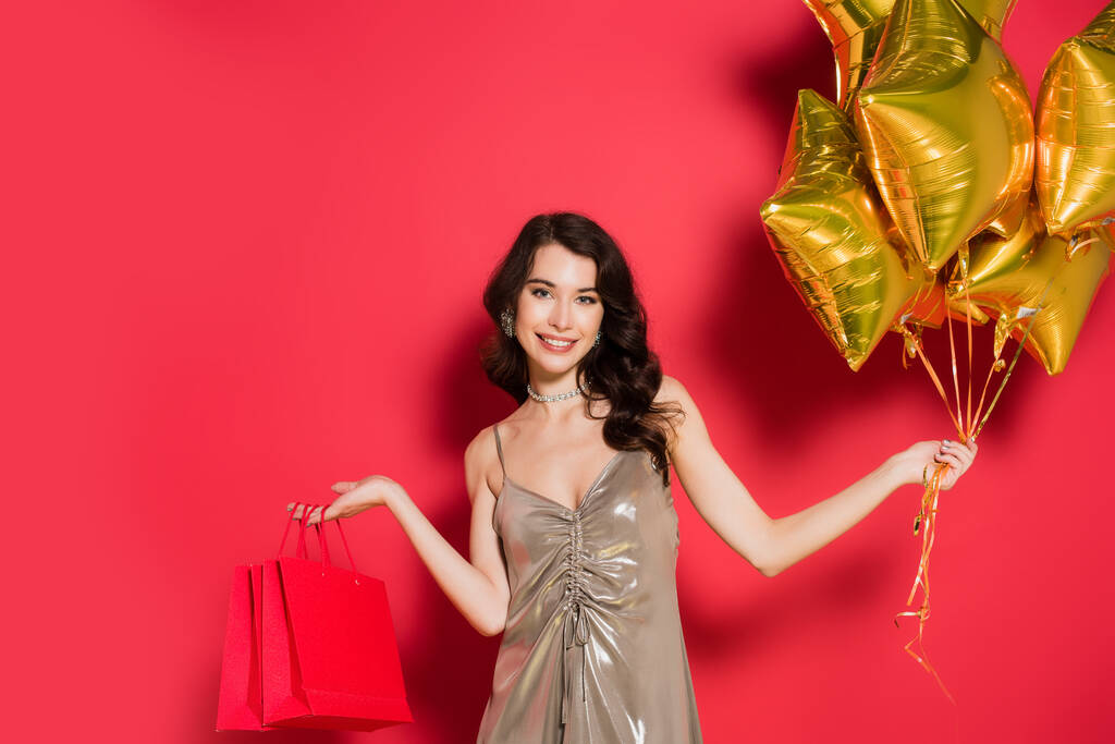 Lächelnde Frau mit Luftballons und Einkaufstüten auf rotem Hintergrund - Foto, Bild
