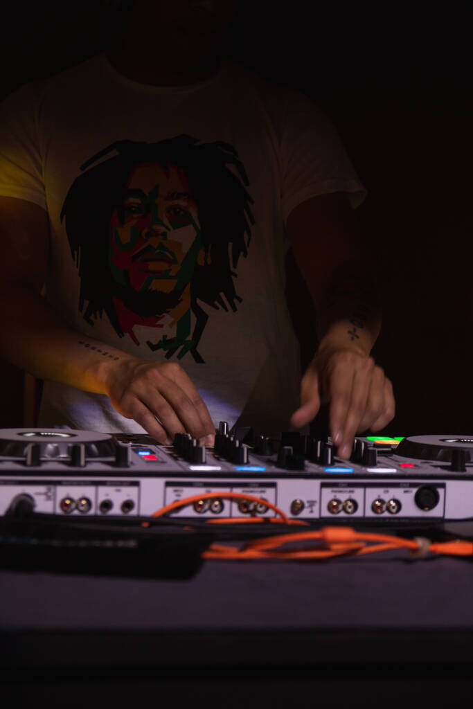 A closeup vertical shot of a man disc jockey mixing music with a controller on turntable in a night club - Photo, Image