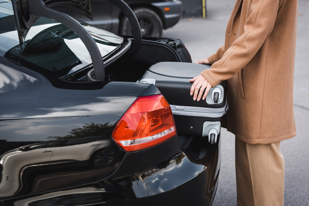 обрезанный вид женщины в осенней одежде положить чемодан в багажник автомобиля - Фото, изображение