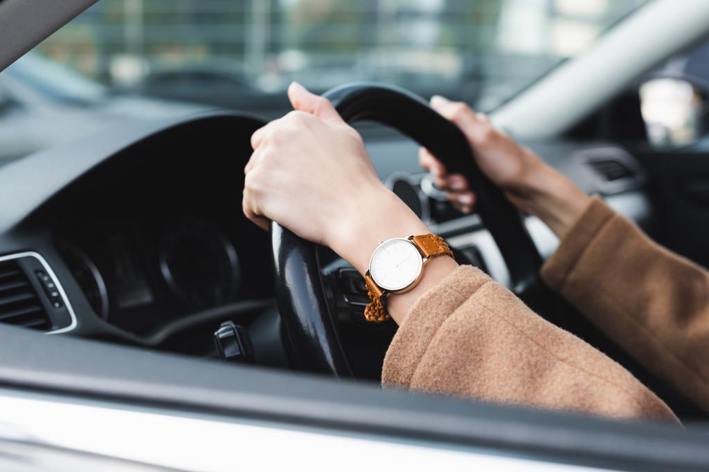 oříznutý pohled na ženu v hodinkách řízení auta na rozmazané popředí - Fotografie, Obrázek