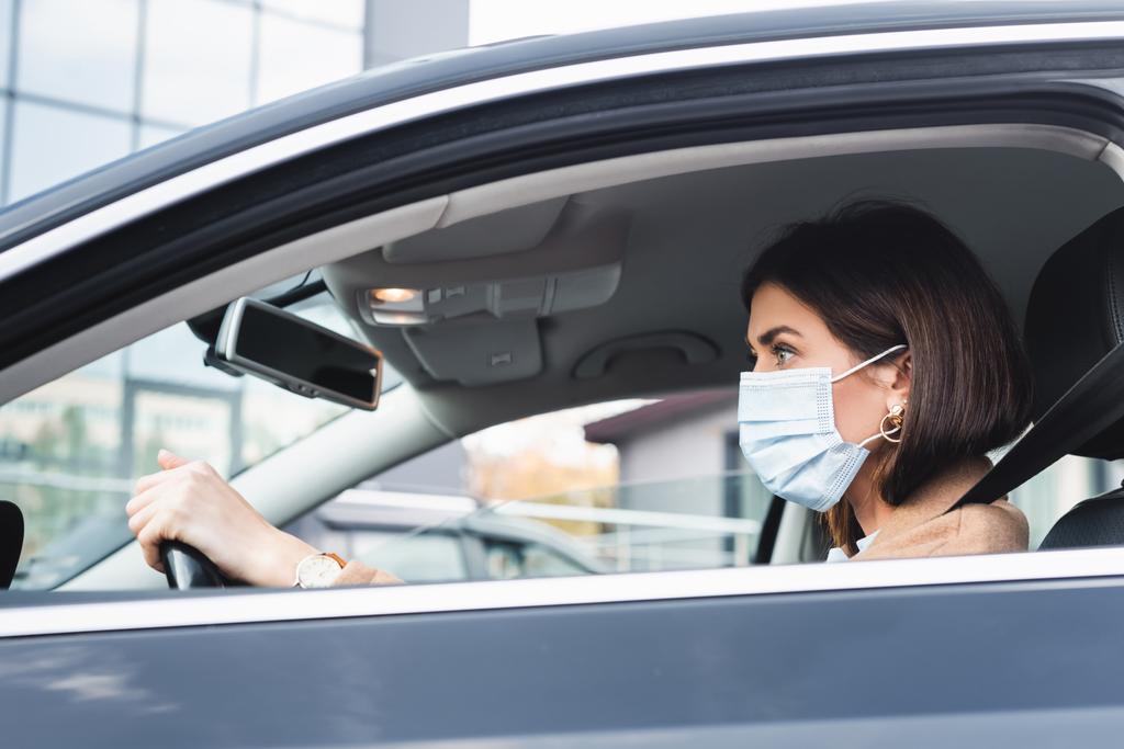 Tıbbi maskeli bir kadın araba kullanırken önüne bakıyor. - Fotoğraf, Görsel