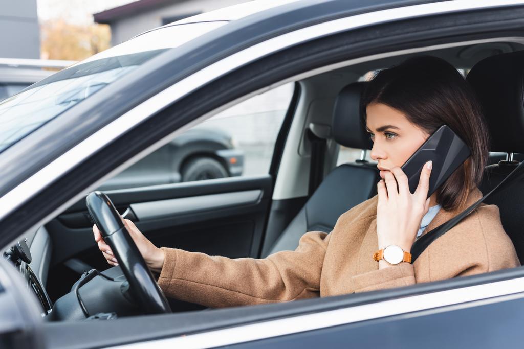 junge Frau fährt Auto und telefoniert mit Handy im unscharfen Vordergrund - Foto, Bild