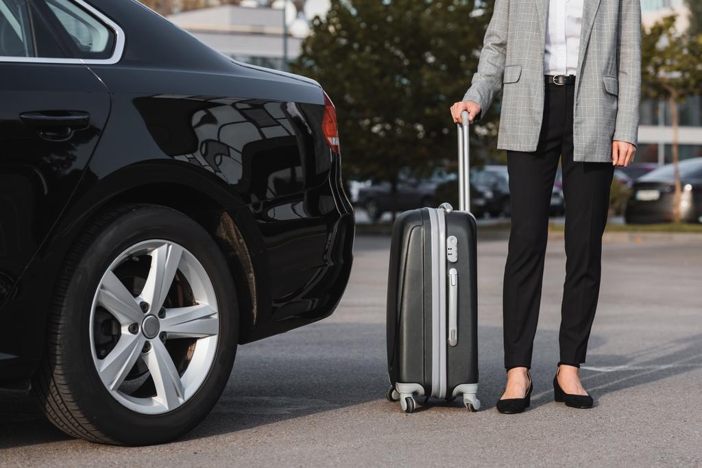 vista recortada de mujer de negocios con maleta cerca de coche negro - Foto, Imagen