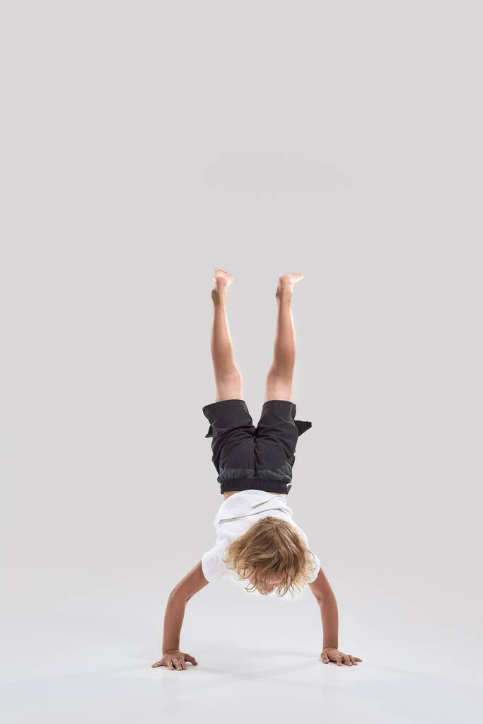 Teljes hossz lövés a kis játékos fiú gyermek áll a karján lábaival felfelé mutató elszigetelt fehér háttér - Fotó, kép