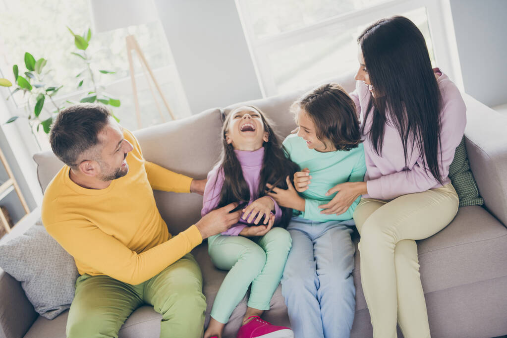 Foto der großen Familie vier Mitglieder sitzen Couch Papa kitzeln Tochter tragen bunte Pullover Hose im Wohnzimmer drinnen - Foto, Bild
