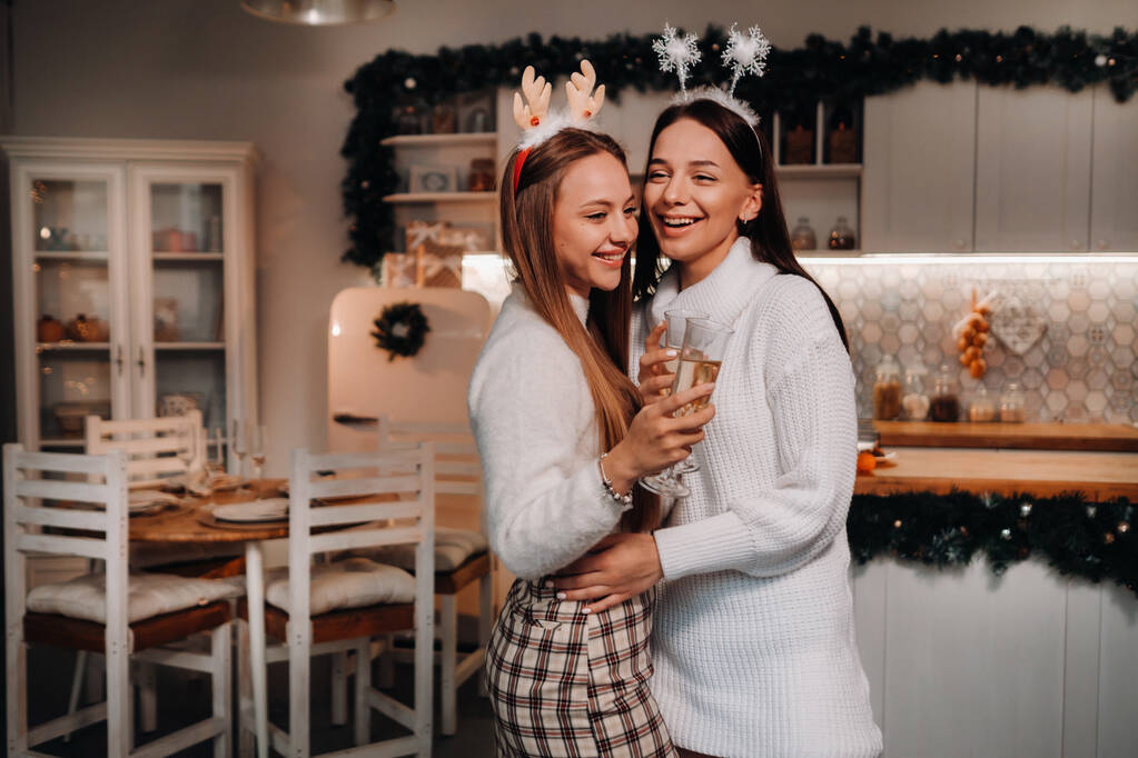 dos chicas en un ambiente acogedor en casa con champán en sus manos en Navidad. Las chicas sonrientes beben champán en una velada festiva - Foto, Imagen