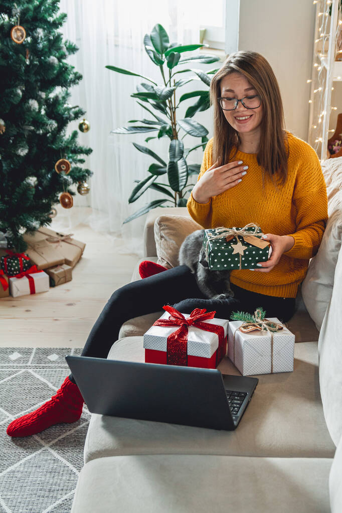 kobieta z laptopem akceptuje online gratulacje Wesołych Świąt i rozpakowuje prezenty - Zdjęcie, obraz