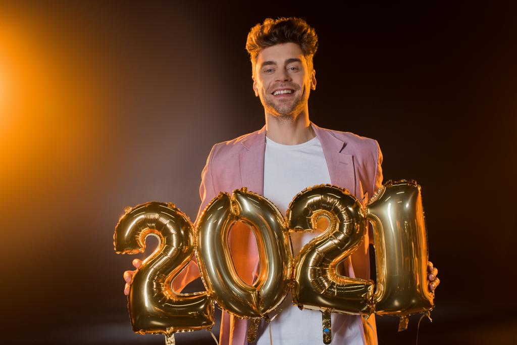 cheerful man holding 2021 numbers balloons on black  - Photo, Image