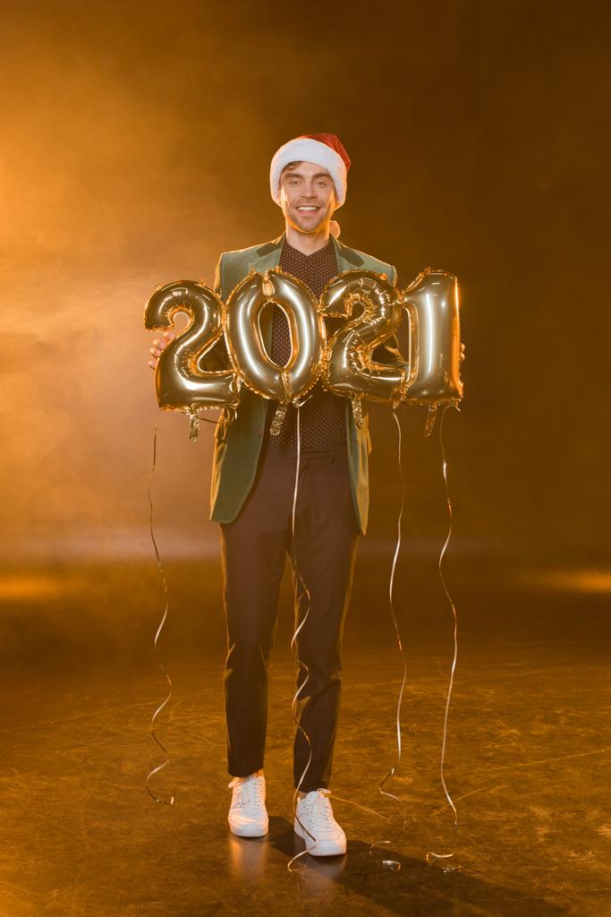 pełna długość szczęśliwy człowiek w Santa kapelusz gospodarstwa balony z 2021 numery na czarny  - Zdjęcie, obraz