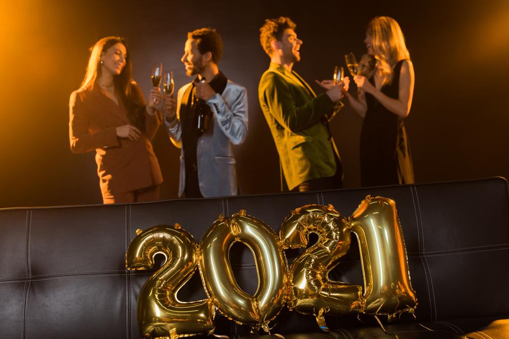 collage de felices amigos multiculturales brindar copas con champán cerca de sofá con 2021 globos sobre fondo negro  - Foto, imagen