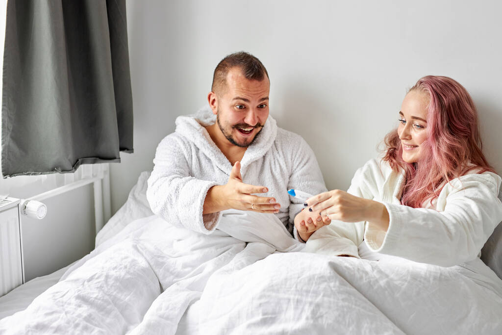 щаслива біла пара схвильована позитивним тестом на вагітність на ліжку
 - Фото, зображення