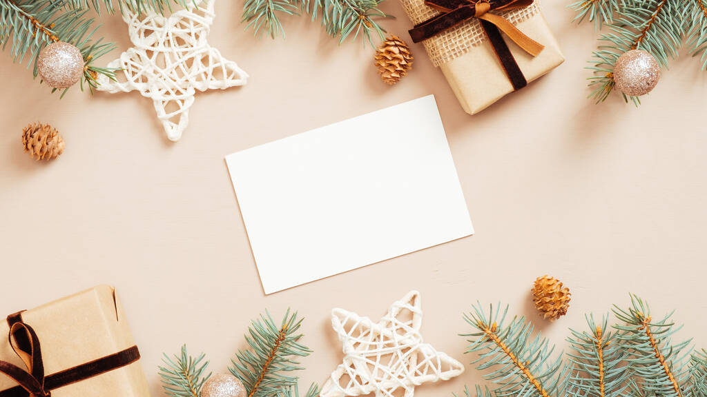 Christmas greeting card mockup on pastel beige background with gift boxes, stars, balls, decorations, fir tree branches. Flat lay, top view. Minimal style. - Photo, Image