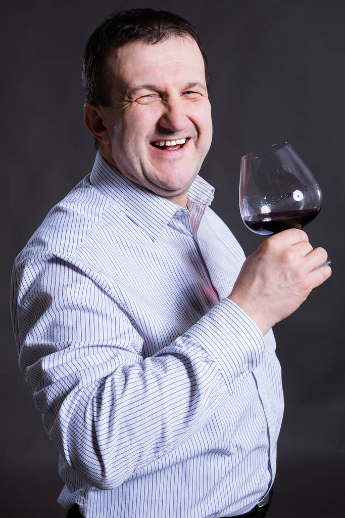 Веселый мужчина средних лет, одетый в рубашку с бокалом вина - Фото, изображение