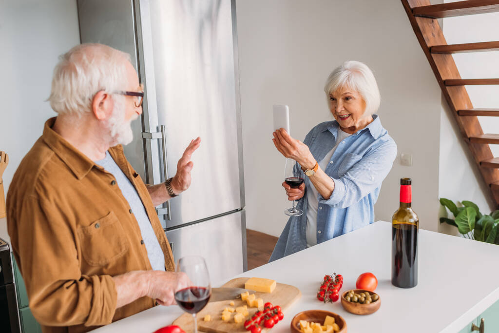 glückliche ältere Frau mit Weinglas und Smartphone beim Kochen von Abendessen in der Küche - Foto, Bild
