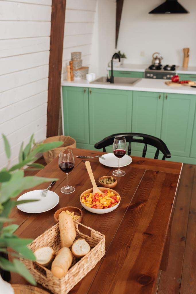 前景にぼやけた植物のキッチンでベジタリアンディナーとワイングラス付きのテーブルを提供しました - 写真・画像
