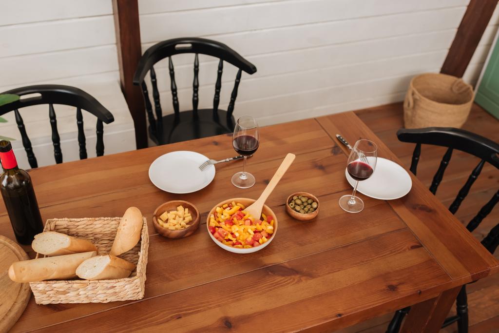 high angle view of served table with vegetarian dinner, baguette in basket and wine in kitchen - Photo, Image