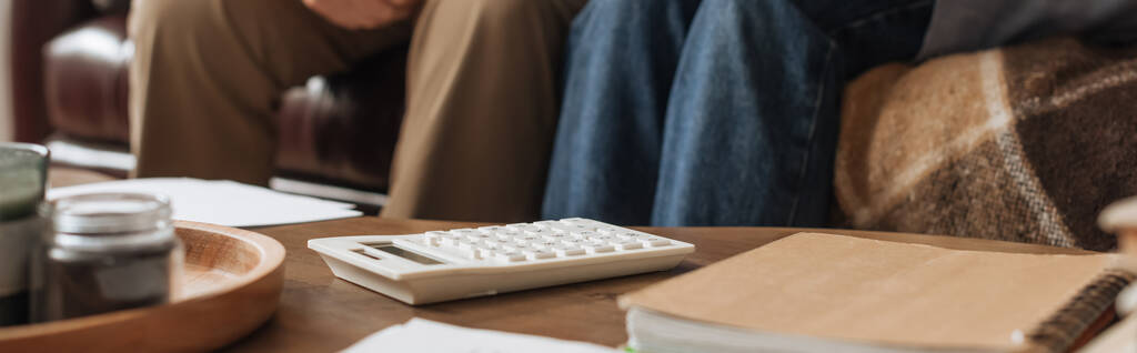 vista cortada de casal de idosos sentado perto da mesa com calculadora branca em casa no fundo borrado, banner - Foto, Imagem