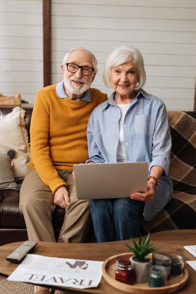 gelukkig ouder paar met laptop kijken naar camera op de bank op wazig voorgrond in de woonkamer - Foto, afbeelding