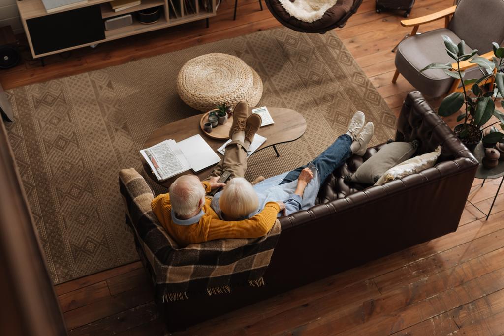 Blick aus der Vogelperspektive auf ein älteres Paar, das sich beim Fernsehen auf der Couch im Wohnzimmer umarmt - Foto, Bild
