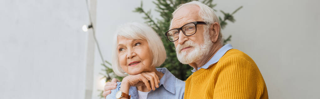 пожилой муж смотрит в сторону, обнимая улыбающуюся жену на террасе на размытом фоне, баннер - Фото, изображение
