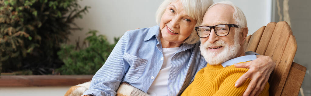 usmívající se starší žena objímající manžela a při pohledu na kameru na terase na rozmazaném pozadí, banner - Fotografie, Obrázek
