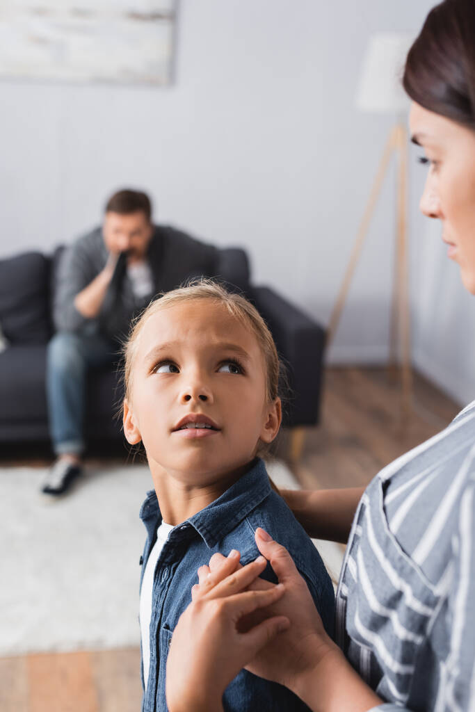 Child looking at mother while abusive father sitting on couch on blurred background  - Photo, Image