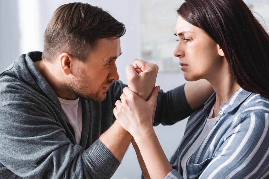 Hombre abusivo mostrando puño a esposa con moretones en casa  - Foto, Imagen