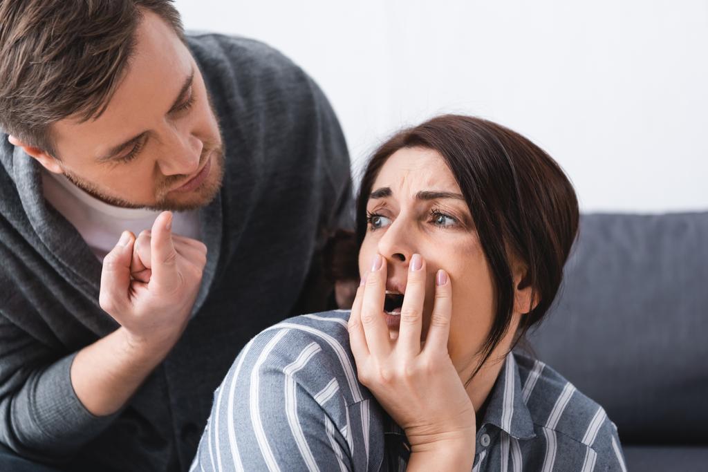 Misshandelter Ehemann zeigt mit Finger auf verängstigte Frau mit Bluterguss auf Wange, der Mund bedeckt  - Foto, Bild