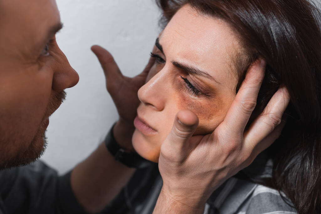 Aggressive man touching face of wife with bruises  - Photo, Image