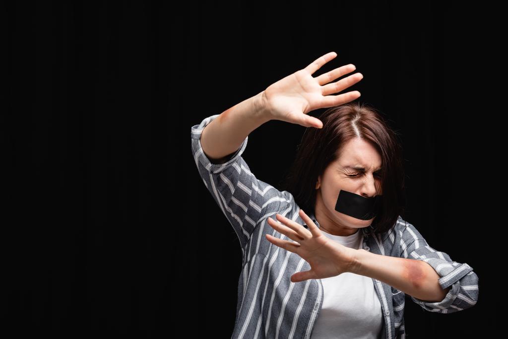 Félős nő horzsolásokkal és ragasztószalaggal, ami fekete alapon izolált stop gesztust mutat.  - Fotó, kép