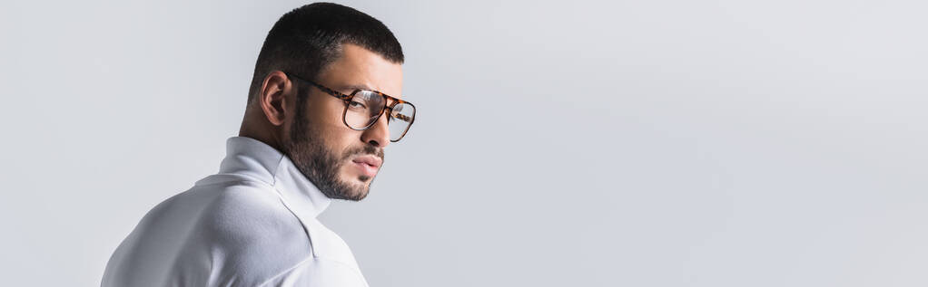 Uomo barbuto in occhiali e dolcevita bianco guardando lontano isolato su grigio, banner  - Foto, immagini