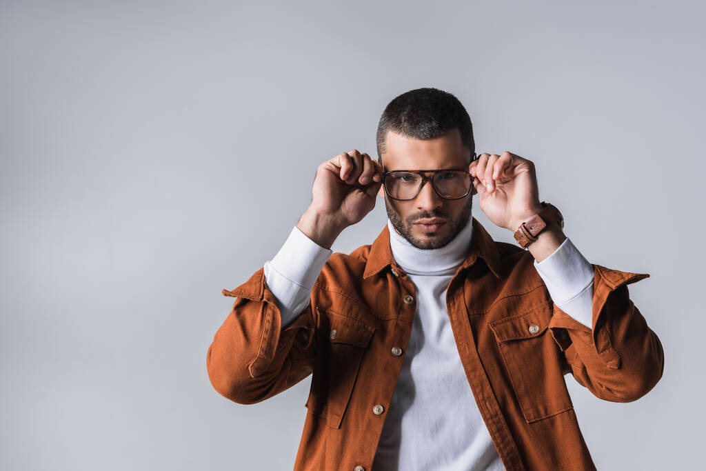 Αυτοπεποίθηση και κομψό άνδρα κρατώντας γυαλιά που απομονώνονται σε γκρι  - Φωτογραφία, εικόνα
