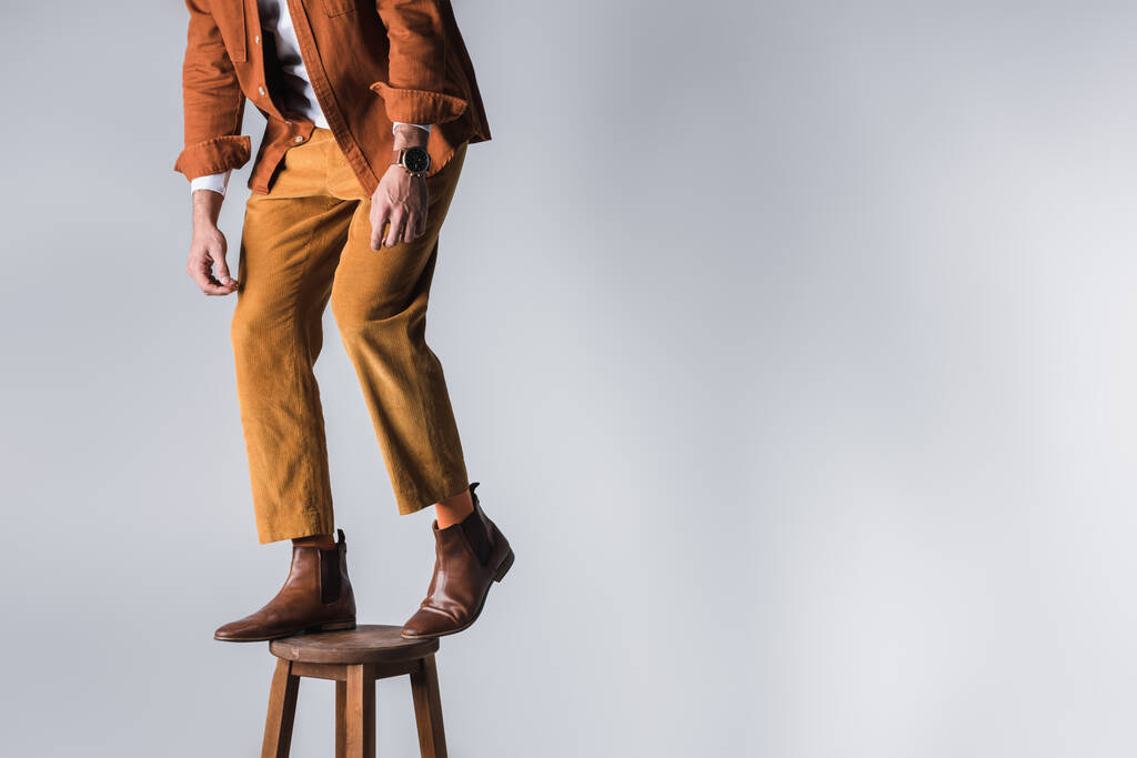 Widok modnego mężczyzny w brązowych butach stojącego na drewnianym krześle na szarym tle  - Zdjęcie, obraz