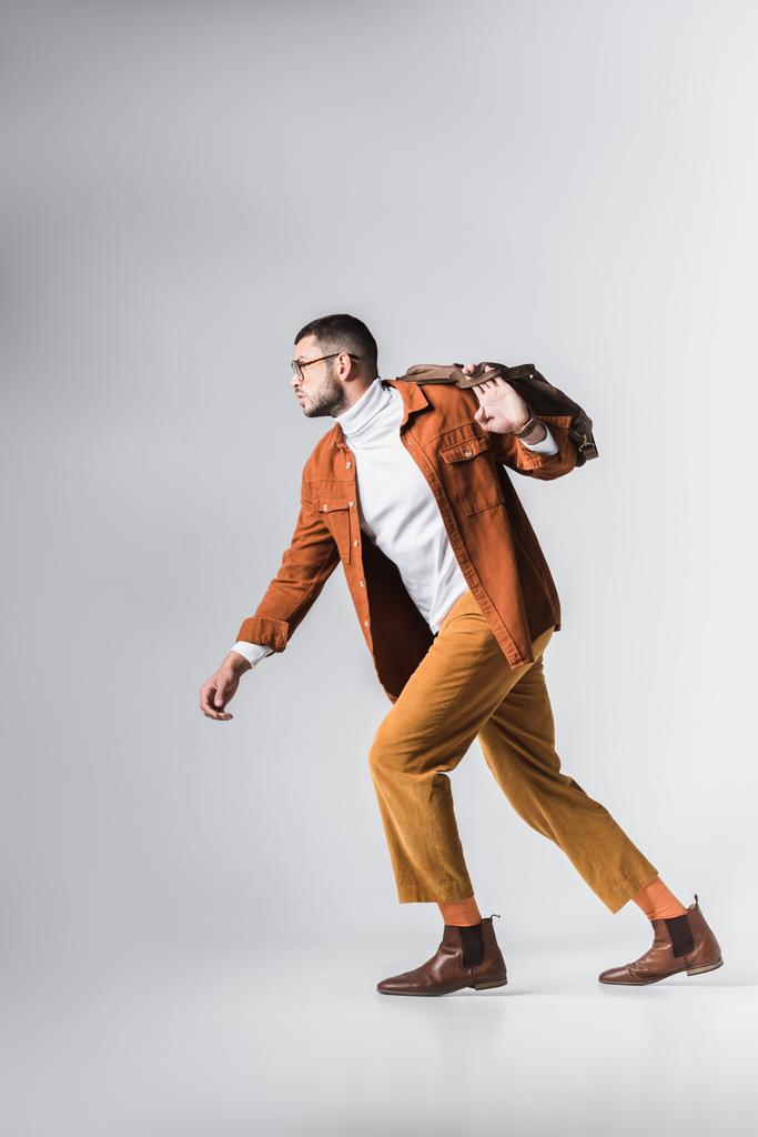 Модный мужчина в очках с коричневой сумкой на сером фоне  - Фото, изображение