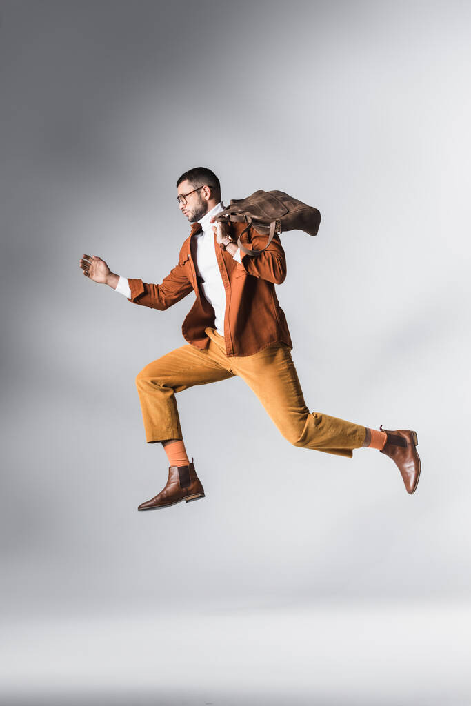 Stilvoller bärtiger Mann mit brauner Tasche in der Luft auf grauem Hintergrund  - Foto, Bild