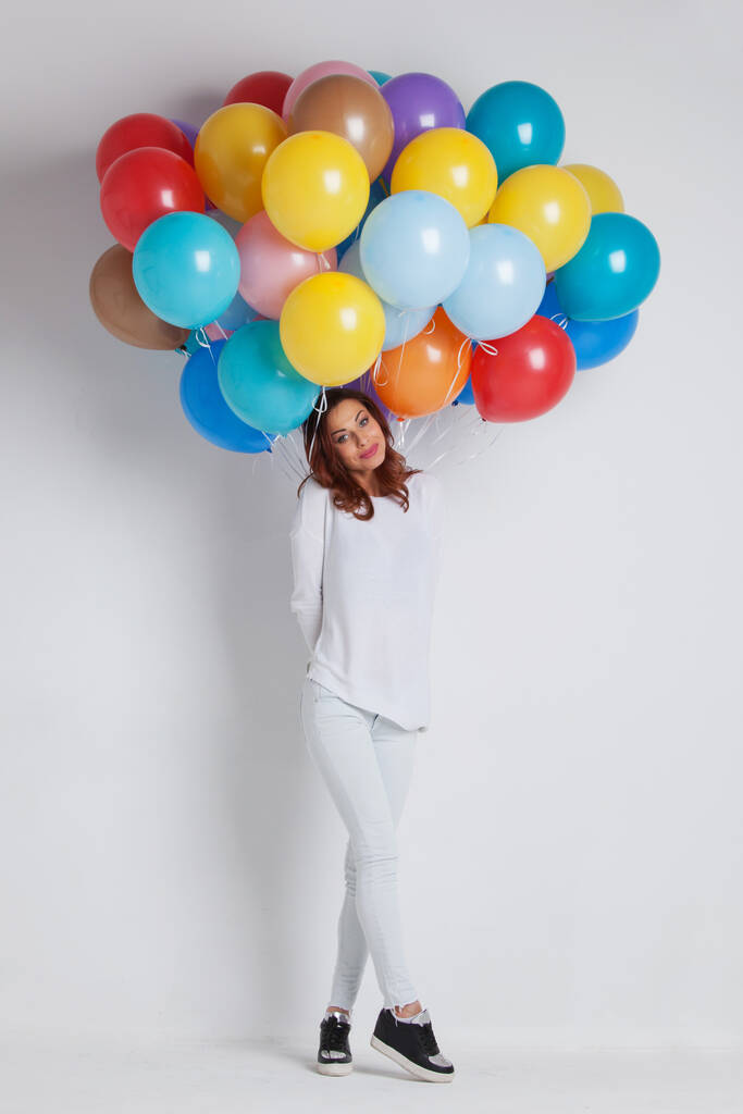 Νεαρή όμορφη γυναίκα σε λευκά ρούχα με χρωματιστά μπαλόνια σε λευκό φόντο με αντίγραφο χώρο για κείμενο - Φωτογραφία, εικόνα