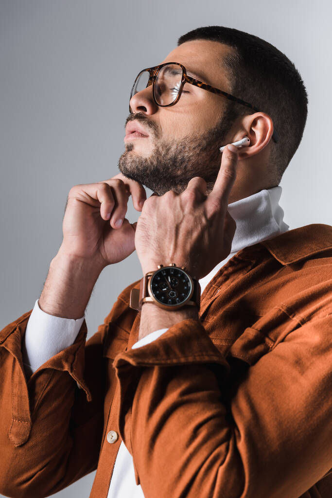 Homem elegante ajustando fone de ouvido no fundo cinza  - Foto, Imagem