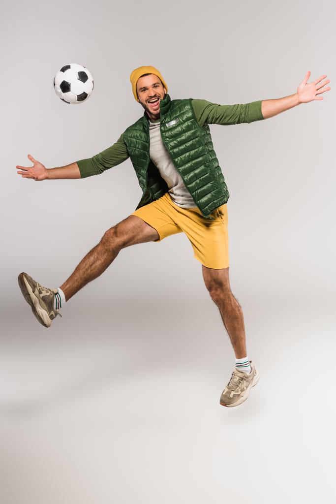 ポジティブな男は灰色の背景で空気中のサッカーの近くにジャンプ ロイヤリティフリー写真 画像素材