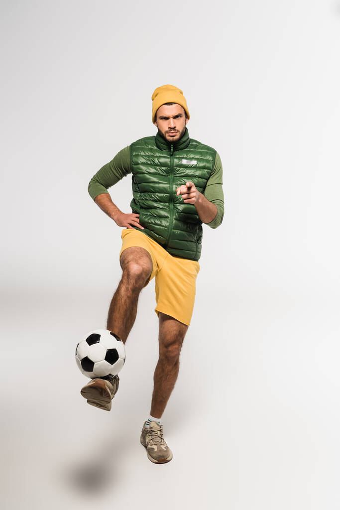 Sportivo serio che punta con il dito alla fotocamera mentre gioca a calcio su sfondo bianco  - Foto, immagini