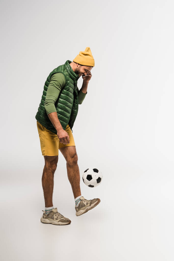 Mosolygós sportoló beszél okostelefonon, és focizik szürke háttér  - Fotó, kép