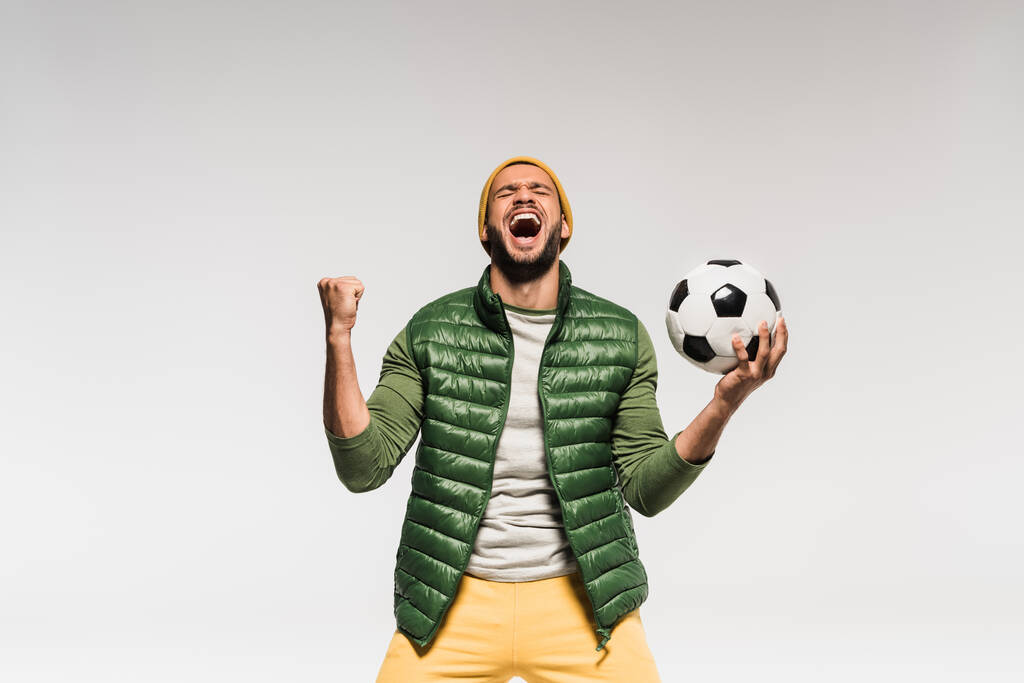 Opgewonden sportman die voetbal vasthoudt en ja-gebaar op grijs laat zien  - Foto, afbeelding