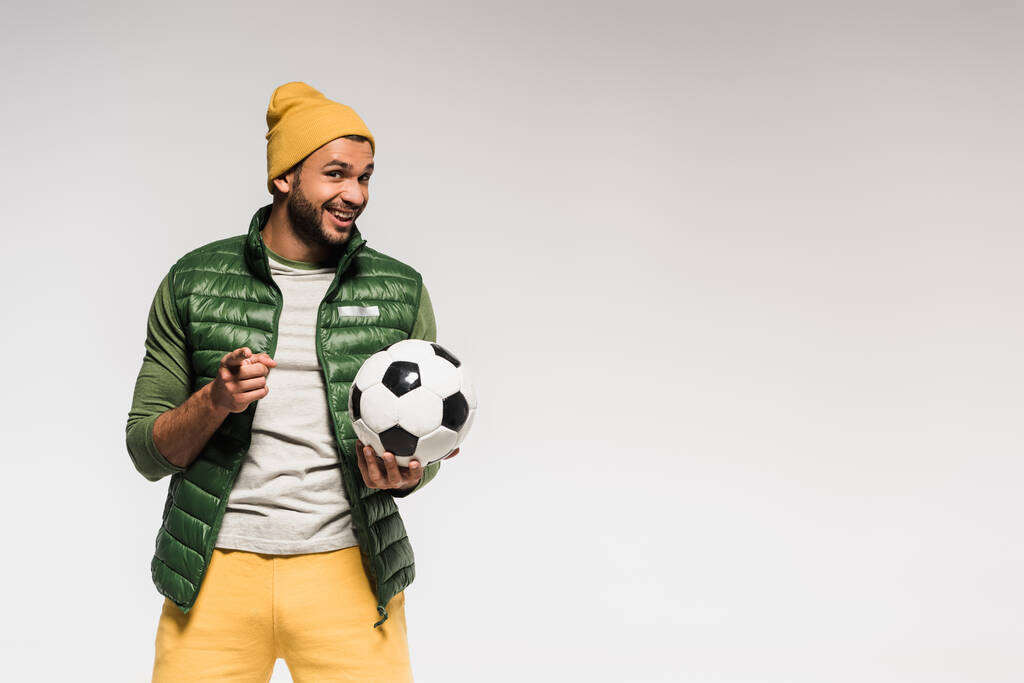 Pozitivní sportovec s míčem ukazujícím prstem na kameru izolovaný na šedi  - Fotografie, Obrázek